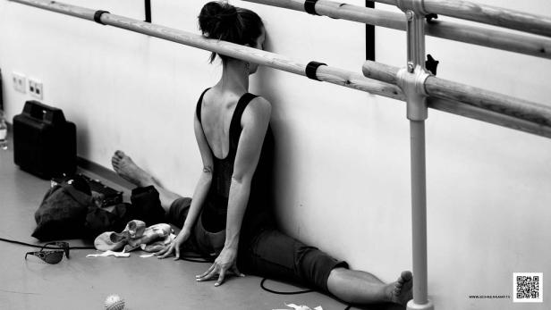 Eine Ballerina dehnt sich an einer Ballettstange in einem Tanzstudio.