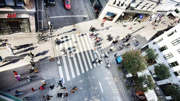 Eine belebte Stadtstraße mit Fußgängern, Radfahrern und Autos von oben gesehen.
