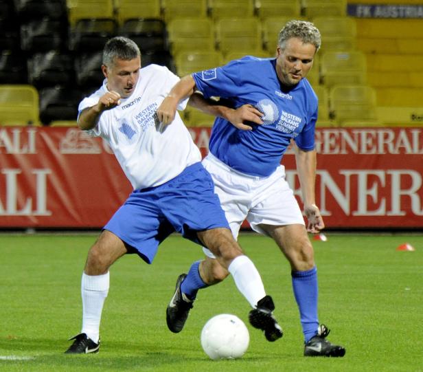 Zwei Männer spielen Fußball auf einem grünen Rasenplatz.