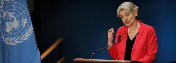 Eine Frau in rotem Blazer spricht am Rednerpult neben der Flagge der Vereinten Nationen.