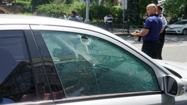Ein Auto mit einem eingeschossenen Fenster und Polizisten im Hintergrund.