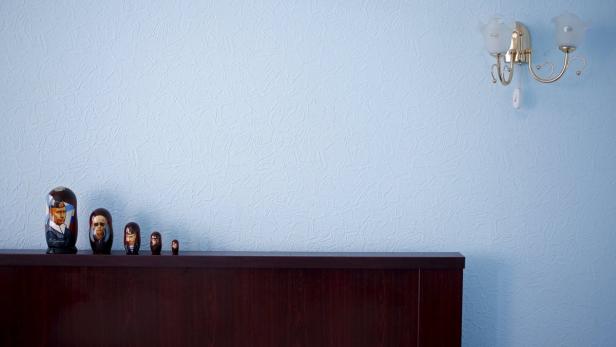 Eine Reihe von Matroschka-Puppen steht auf einem dunklen Holzschrank vor einer blauen Wand.