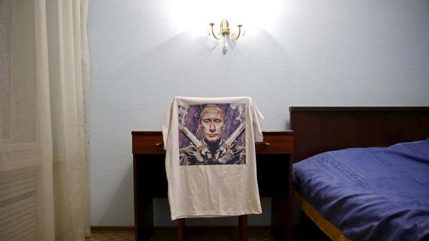 Ein T-Shirt mit einem Bild von Wladimir Putin, der zwei Pistolen hält, liegt auf einem Tisch in einem Schlafzimmer.