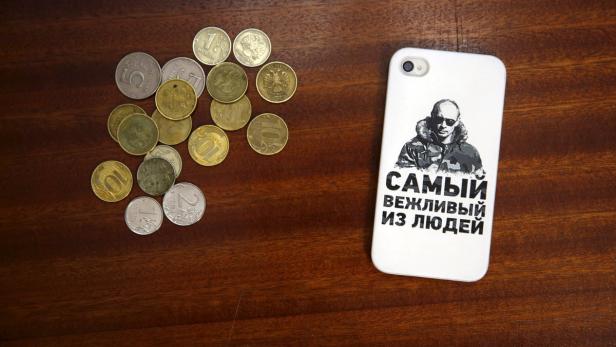 Auf einem Tisch liegen russische Münzen und ein Handy mit einem Bild von Wladimir Putin.