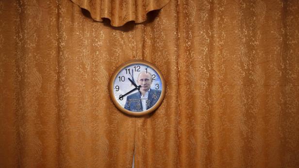 Eine Uhr mit dem Bild von Wladimir Putin hängt an einer goldenen Gardine.