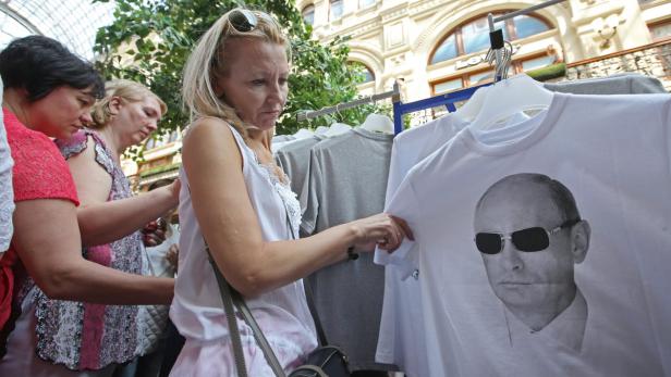 Eine Frau betrachtet ein weißes T-Shirt mit dem Aufdruck von Wladimir Putin mit Sonnenbrille.