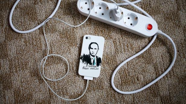 Ein iPhone mit einem Putin-Porträt wird über ein Verlängerungskabel aufgeladen.
