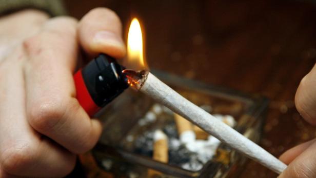 Eine Hand zündet eine Zigarette mit einem Feuerzeug an.