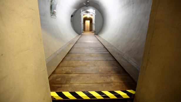 Ein hölzerner Gang führt durch einen Tunnel mit gelb-schwarzer Warnmarkierung.