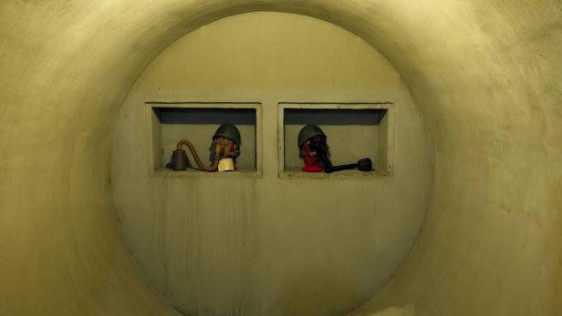 Zwei Gasmasken mit Helmen sind in Nischen in einer Tunnelwand ausgestellt.