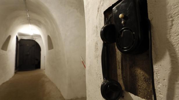 Ein altes, schwarzes Telefon hängt an einer Wand in einem unterirdischen Gang.