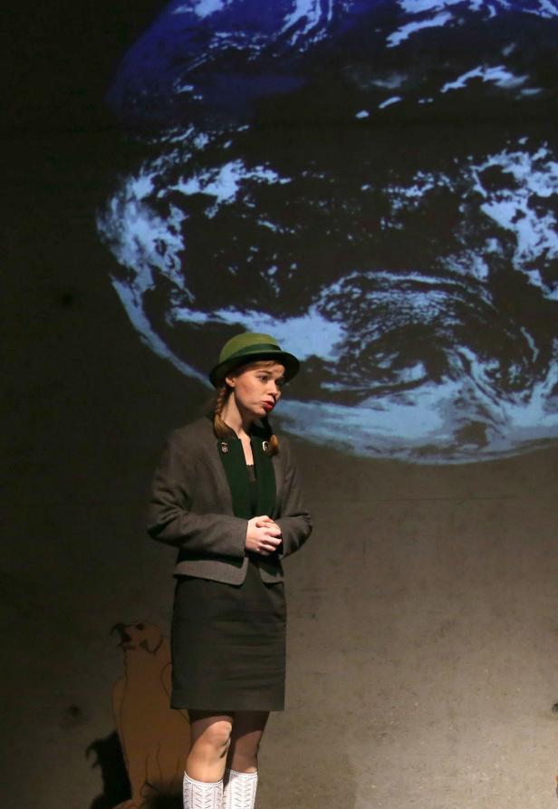 Eine Frau mit Hut steht vor einer Projektion der Erde.