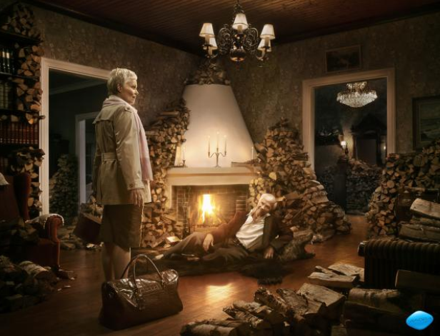 Ein älteres Paar in einem mit Holzscheiten dekorierten Wohnzimmer vor einem Kamin.