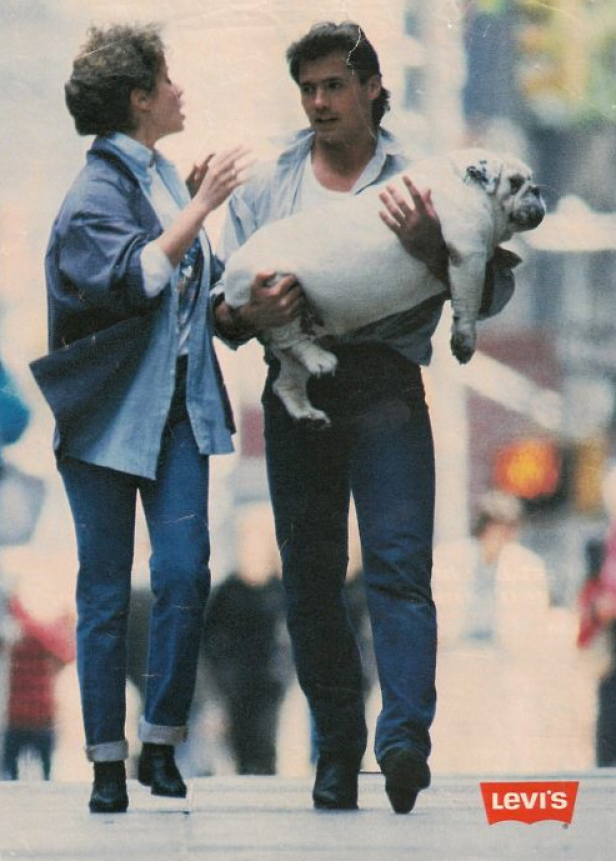 Ein Mann trägt einen Bulldog auf einer belebten Straße, während eine Frau neben ihm geht.