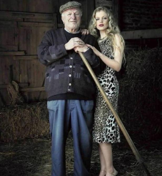 Ein älterer Mann mit Mütze und eine junge Frau im Leopardenkleid posieren in einer Scheune.