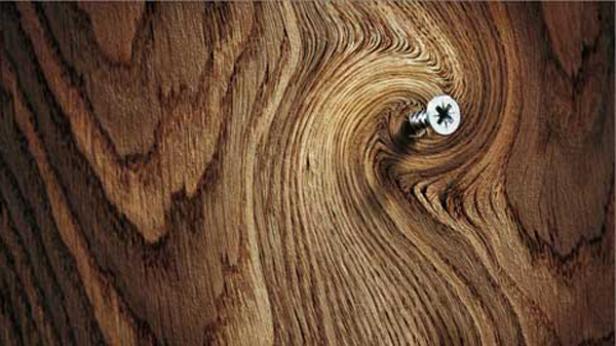 Eine Schraube steckt in einem Stück Holz mit auffälliger Maserung.