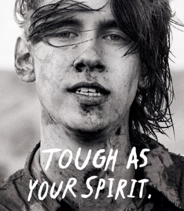 Ein junger Mann mit Schmutz im Gesicht blickt ernst in die Kamera.