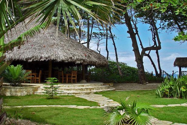Ein strohgedecktes Gebäude mit Tischen und Stühlen in einer tropischen Umgebung.