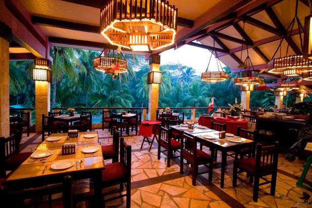 Ein Restaurant mit Tischen und Stühlen im Freien, umgeben von Palmen.