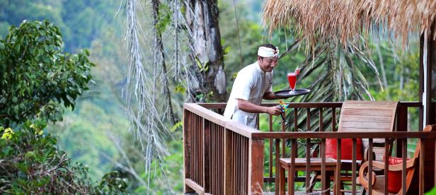 Ein Kellner serviert Getränke auf einer Terrasse mit Blick auf üppiges Grün.