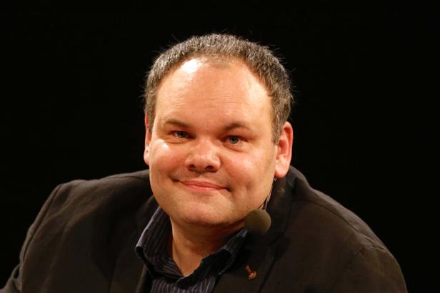 Ein Mann mit Mikrofon lächelt in die Kamera.