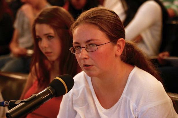 Eine junge Frau spricht in ein Mikrofon vor einem Publikum.