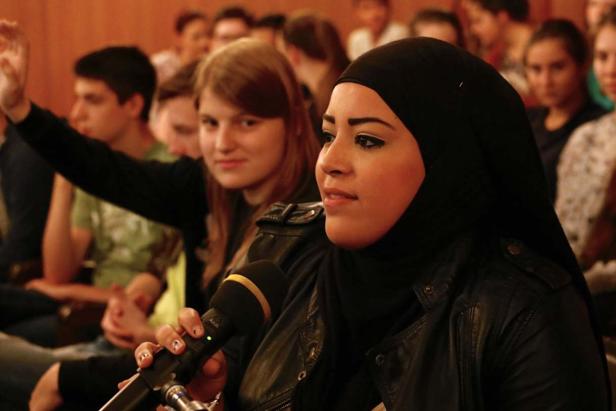 Eine Frau mit Hijab spricht in ein Mikrofon vor einem Publikum.