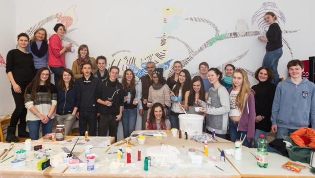Eine Gruppe von Schülern und Lehrern steht vor einem Wandbild und bemalen es.