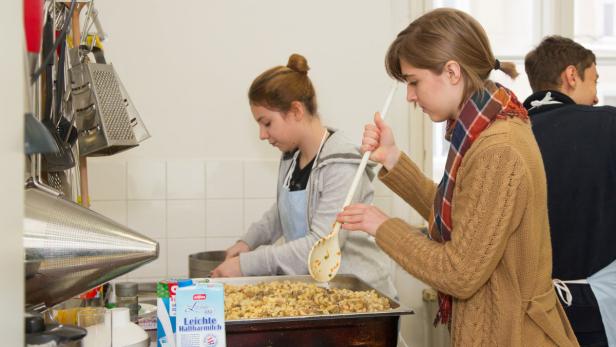 Zwei junge Frauen bereiten in einer Küche ein Gericht mit Nudeln zu.