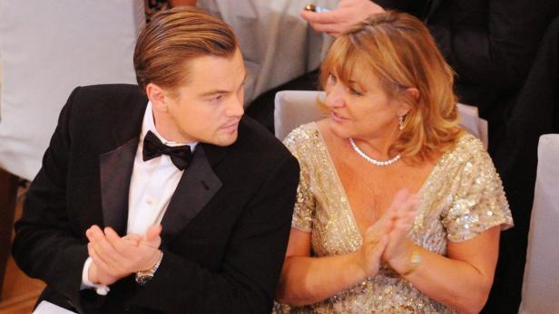 Leonardo DiCaprio sitzt neben einer Frau in einem goldenen Kleid und klatscht Beifall.