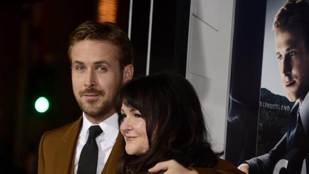 Ryan Gosling mit einer Frau auf dem roten Teppich vor einem Plakat mit seinem Bild.