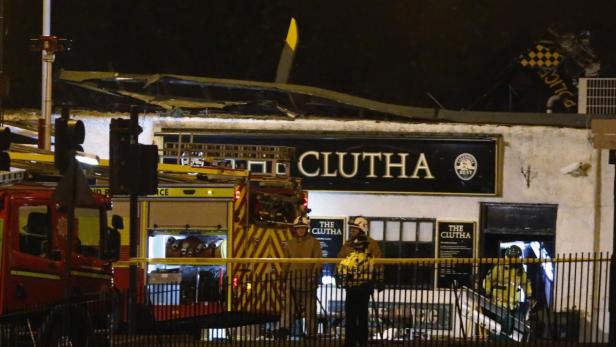 Feuerwehrleute stehen vor dem beschädigten „Clutha“-Pub in der Nacht.