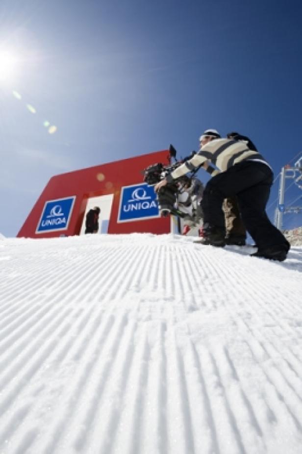 Ein Kameramann filmt auf einer Skipiste vor einem roten Torbogen mit dem Uniqua-Logo.