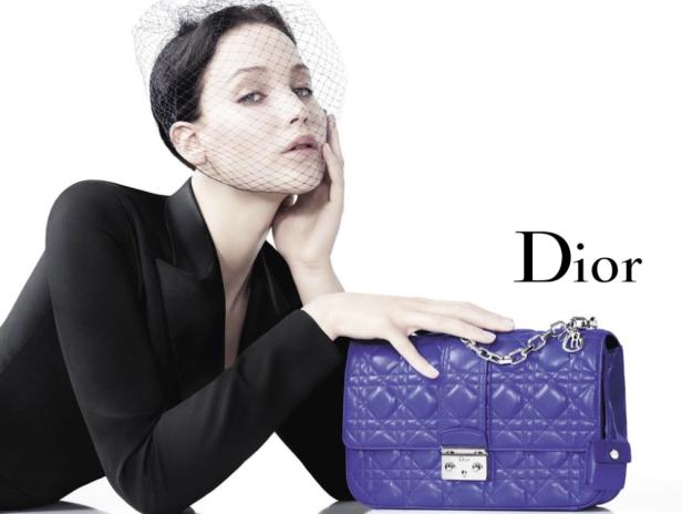 Eine Frau mit Schleier präsentiert eine blaue „Dior“-Handtasche.