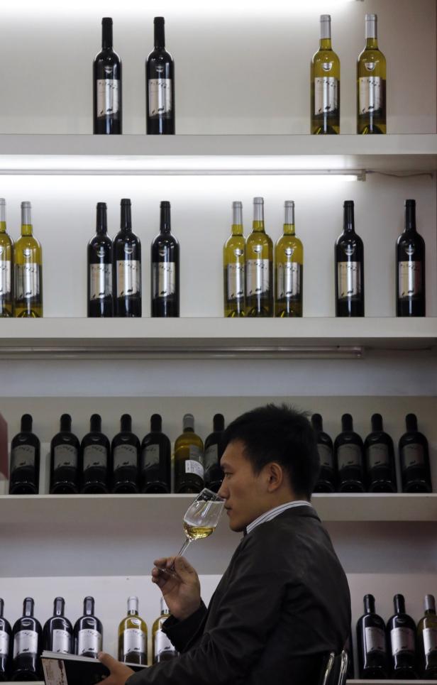 Ein Mann in einem Weinladen verkostet Weißwein vor Regalen voller Weinflaschen.