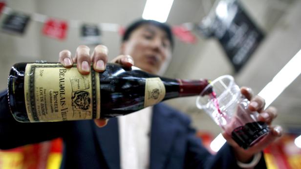 Eine Person gießt Beaujolais-Wein in einen Plastikbecher.