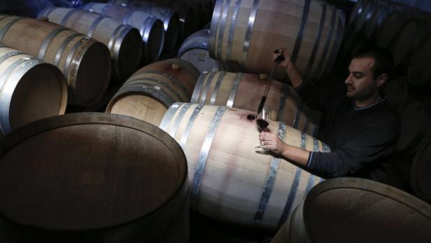 Ein Mann probiert Wein aus einem Fass in einem Weinkeller.