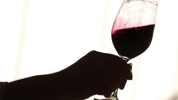 Eine Hand hält ein Glas Rotwein gegen einen hellen Hintergrund.