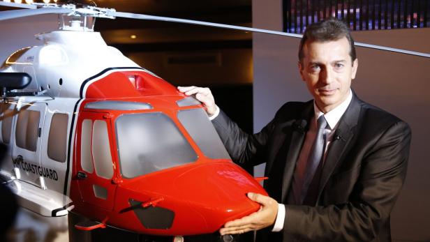 Ein Mann im Anzug präsentiert ein Modell eines rot-weißen Küstenwachen-Hubschraubers.