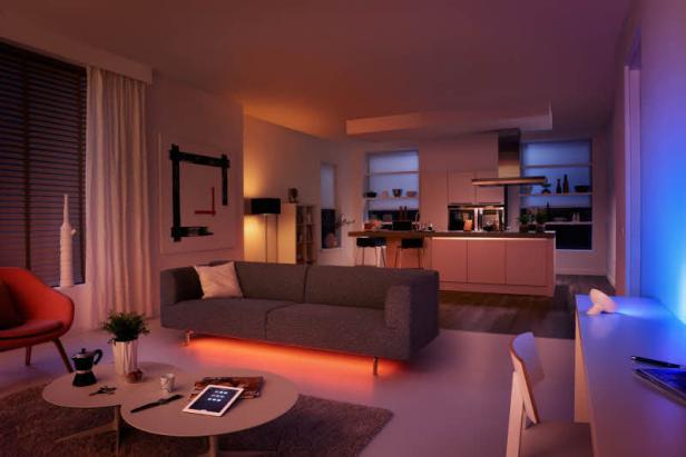 Ein modernes Wohnzimmer mit Sofa, Couchtisch und offener Küche, beleuchtet mit farbigen Lichtern.