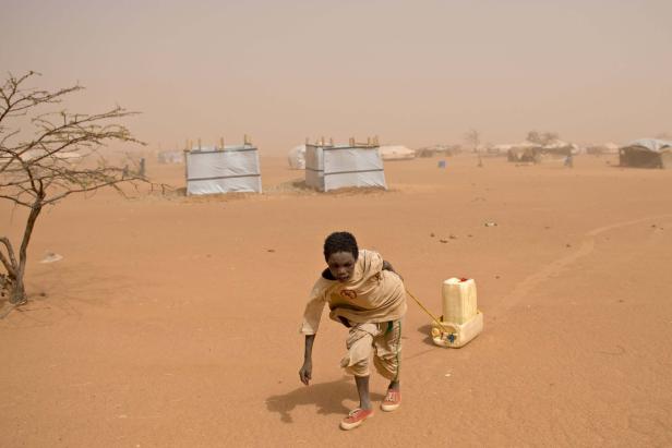 Ein Junge zieht einen Wasserkanister durch ein staubiges Flüchtlingslager.