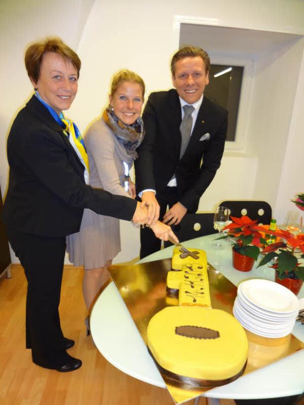 Drei Personen schneiden gemeinsam eine gelbe Gitarren-Torte an.