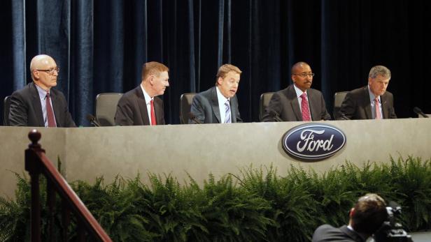 Fünf Männer sitzen an einem Tisch mit dem Ford-Logo im Hintergrund.