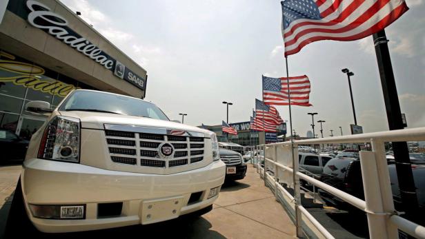 Ein weißer Cadillac steht vor einem Autohaus mit amerikanischen Flaggen.