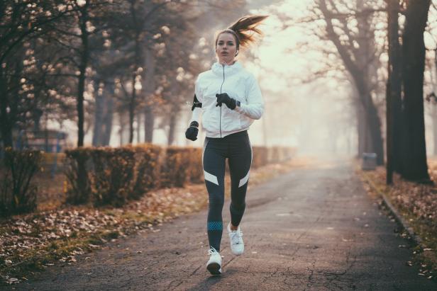 Eine Frau joggt an einem nebligen Tag auf einem Weg mit Bäumen.