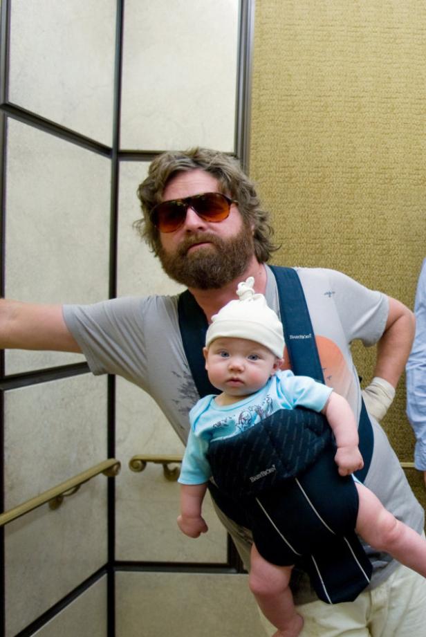Zach Galifianakis mit Sonnenbrille und Babytrage mit einem Baby darin.