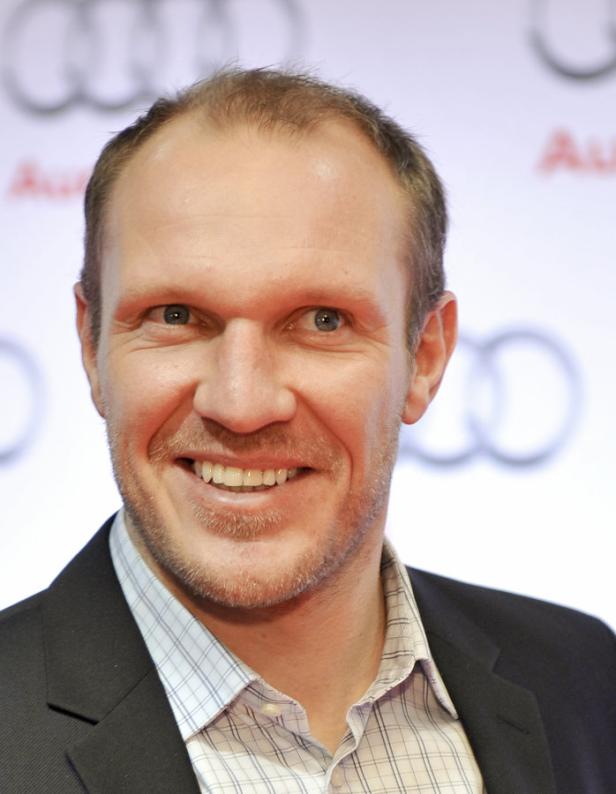 Ein lächelnder Mann im Anzug vor einem Audi-Logo.