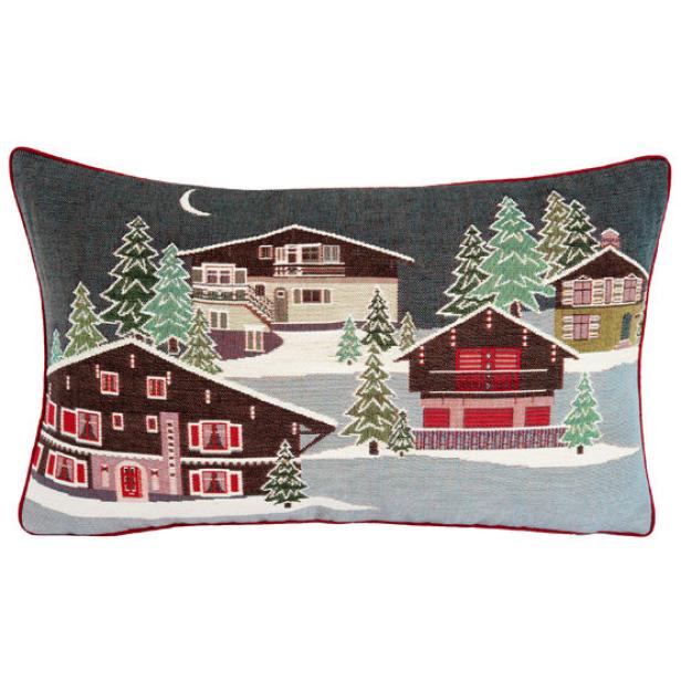 Ein Kissen mit dem Motiv einer verschneiten Winterlandschaft mit Häusern und Tannenbäumen bei Nacht.