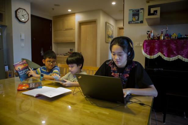 Ein Kind mit Buch, eines mit Heft und eine Jugendliche mit Laptop lernen zu Hause
