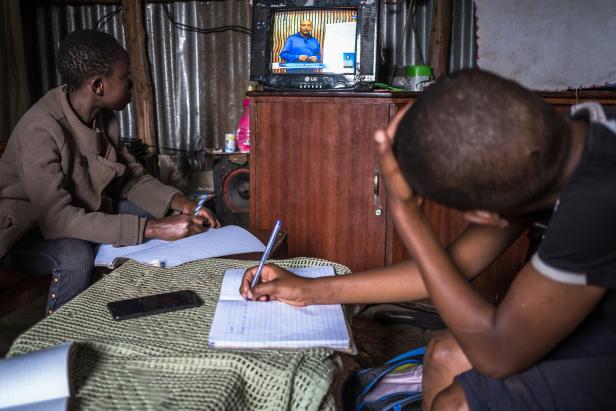 Zwei Jugendliche schauen Bildugnsfernsehen in Nairobi (Kenya) und schreiben in ihre Hefte